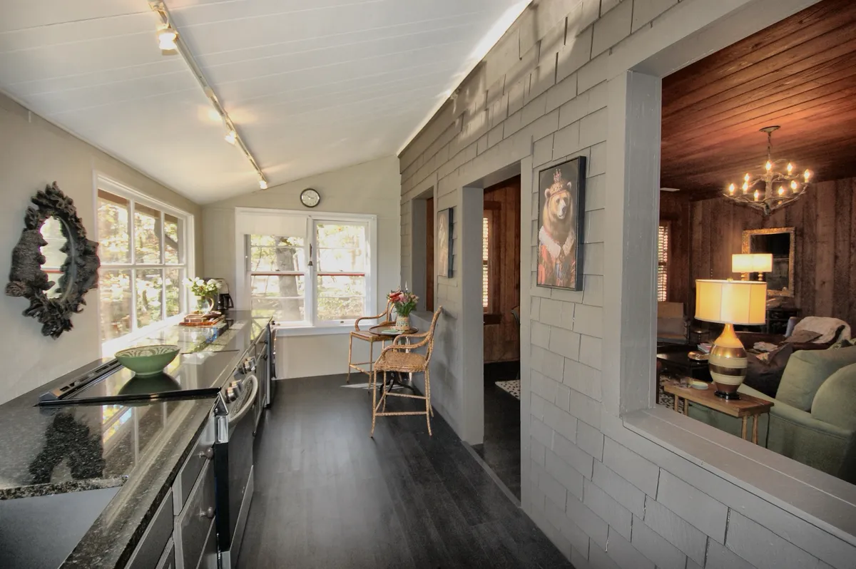 An inviting kitchen and seating area with a large countertop, expansive windows letting in natural light, wall art, and a cozy spot for socializing. The setup encourages interaction and relaxation, and the design visually connects the kitchen to an adjacent dining or living space.