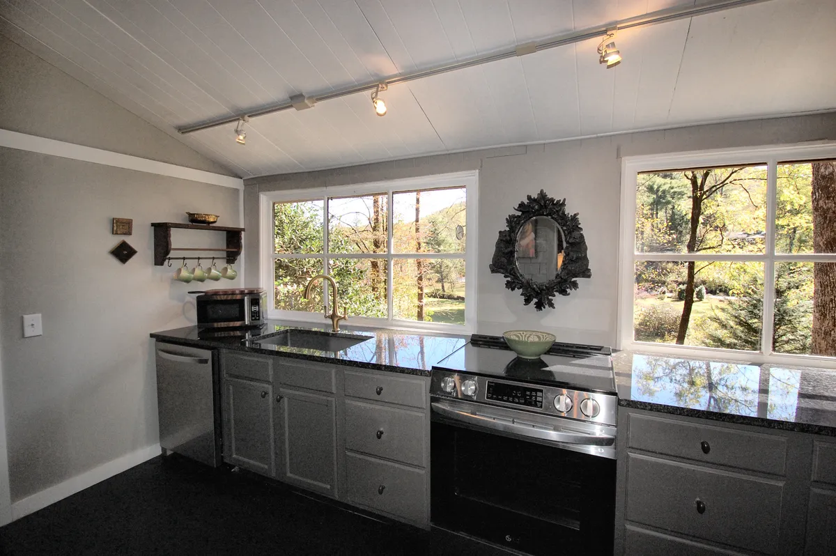A warm kitchen scene with ample countertops, a window revealing a lush landscape, vintage accents such as a decorative mirror and faucet, and subtle hints of classic cabinetry. The space feels both functional and inviting, ideal for gatherings or quiet mornings.
