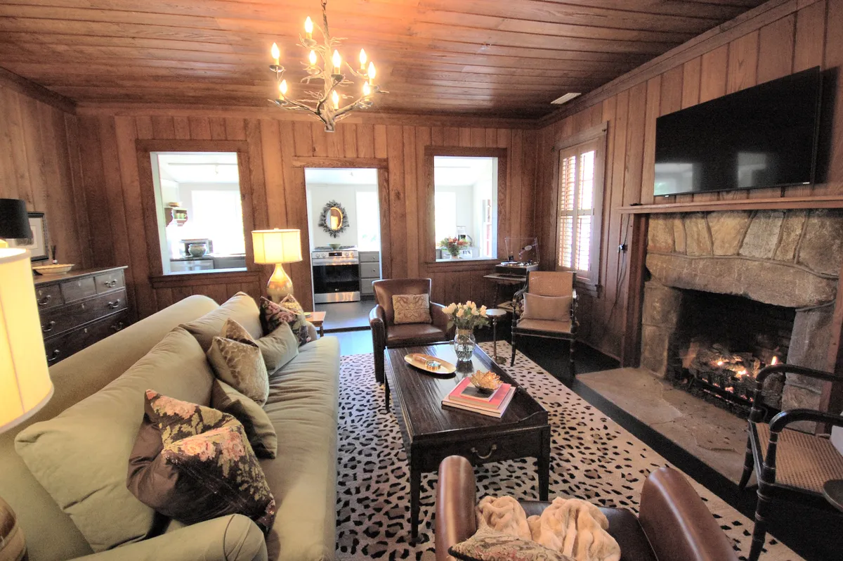 A living space showcasing a distinctive green sofa and a rugged stone fireplace, topped with a classic chandelier. The room is furnished for both relaxation and entertaining, with a coffee table perfect for sharing stories or enjoying a warm drink, enhanced by inviting lighting and vintage-inspired decor.