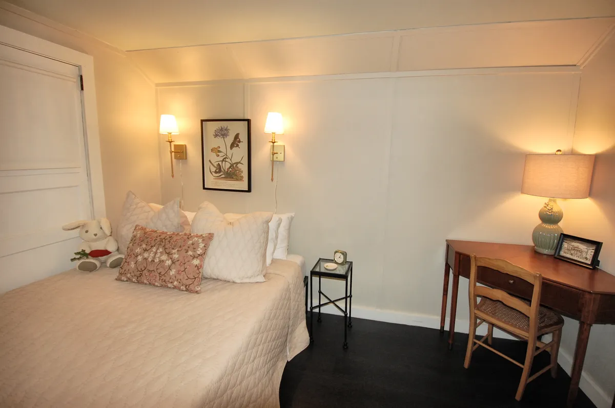 A cozy bedroom with a neatly made bed, a writing desk beside it, a lamp, playful artwork on the wall, and a teddy bear that adds a whimsical, welcoming touch. The atmosphere is calm and inviting, perfect for guests of all ages.