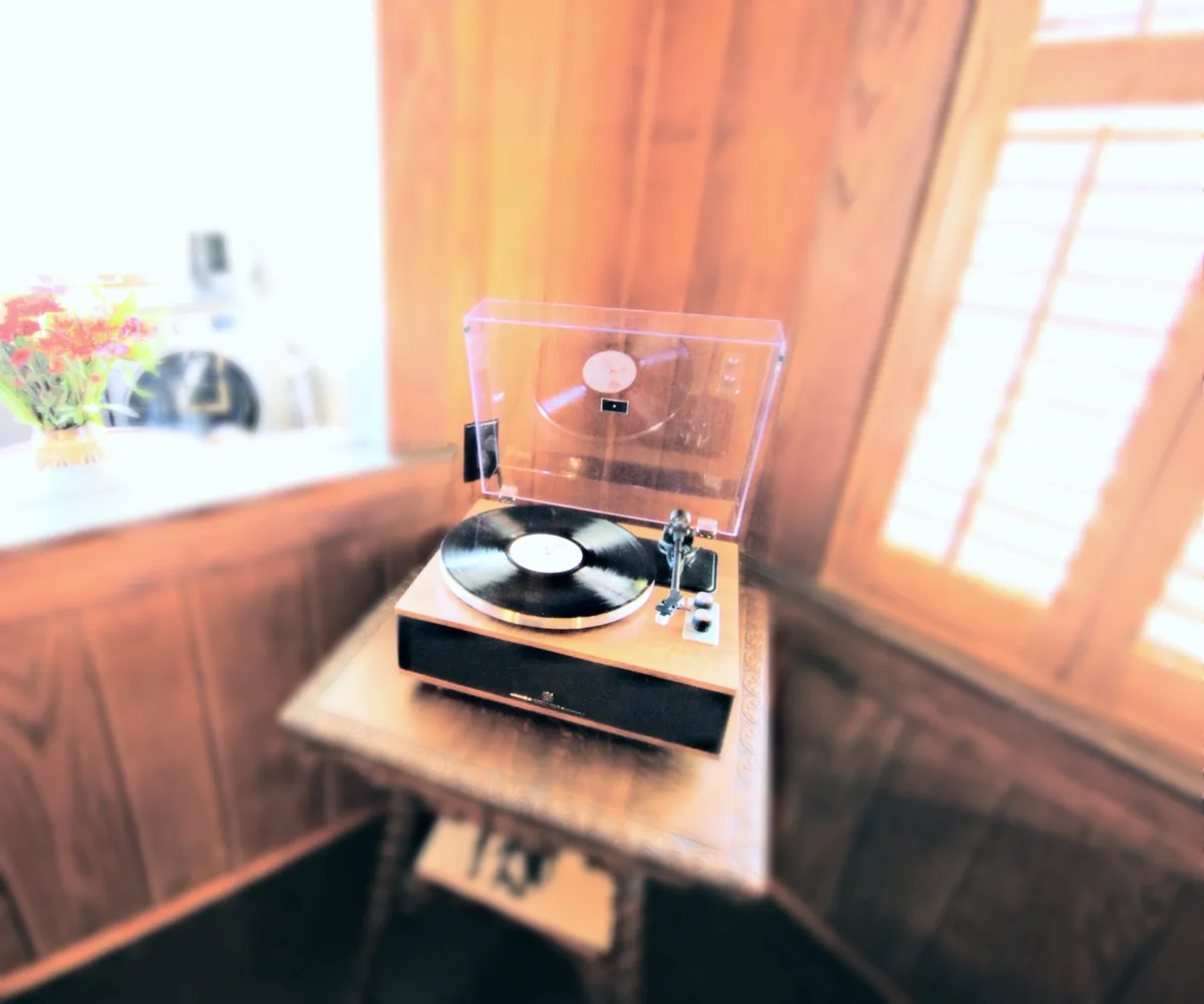 A close-up vignette of a vintage record player atop a wooden table, adorned with a fresh vase of flowers. The nostalgic setup invites guests to spin a classic record, capturing the essence of curated, memorable gatherings.