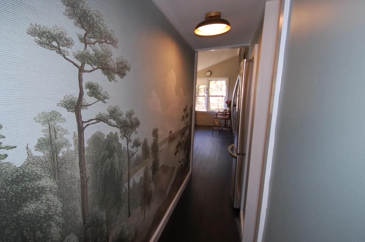 This interior shot features a hallway with a wall mural depicting trees, complemented by soft natural light and a glimpse of the kitchen beyond. The mural brings the outdoors inside, and the tranquil atmosphere invites exploration of the home after returning from outdoor adventures.