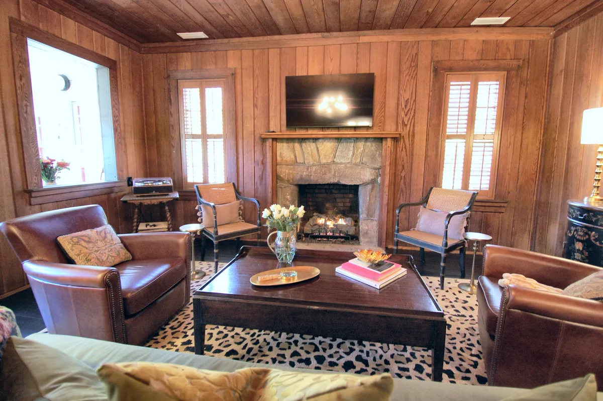 A warmly lit living room centers on a vintage-inspired gas log fireplace, with comfortable seating and large windows revealing glimpses of the outdoors. The inviting ambience is perfect for cozy evenings spent together after a day of exploration.